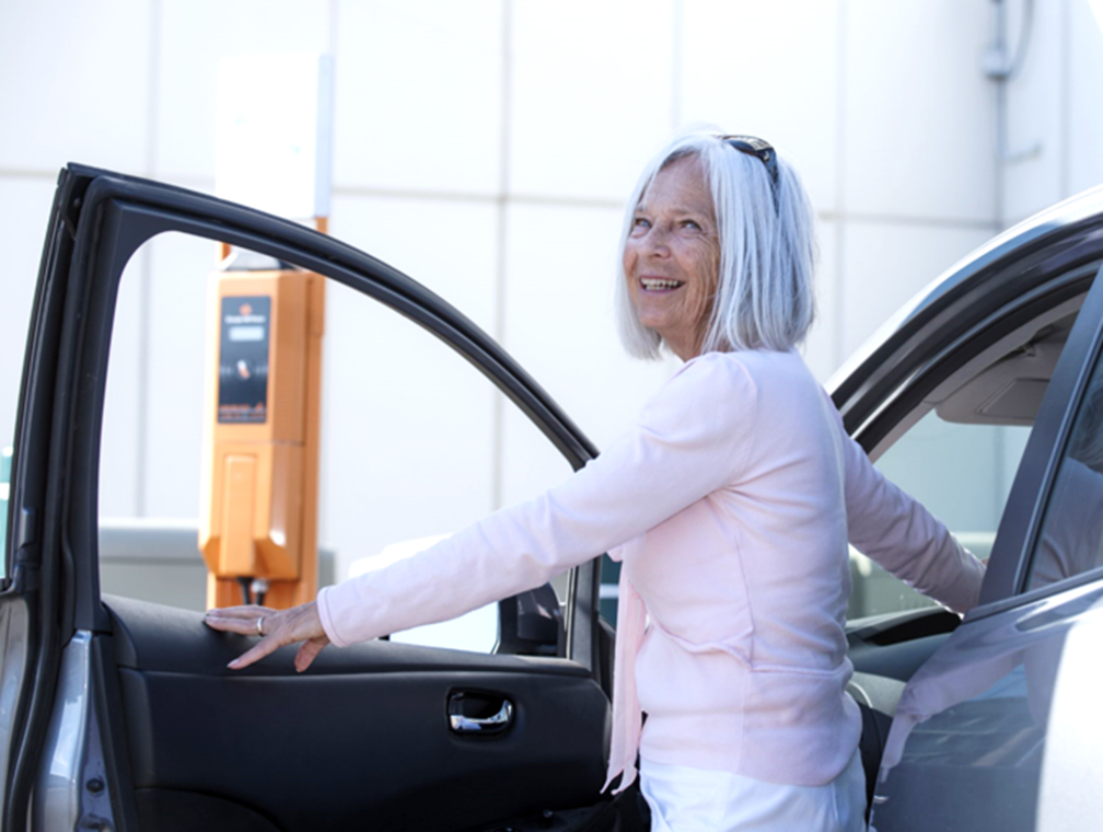 Retired woman steps out of her car near charging station